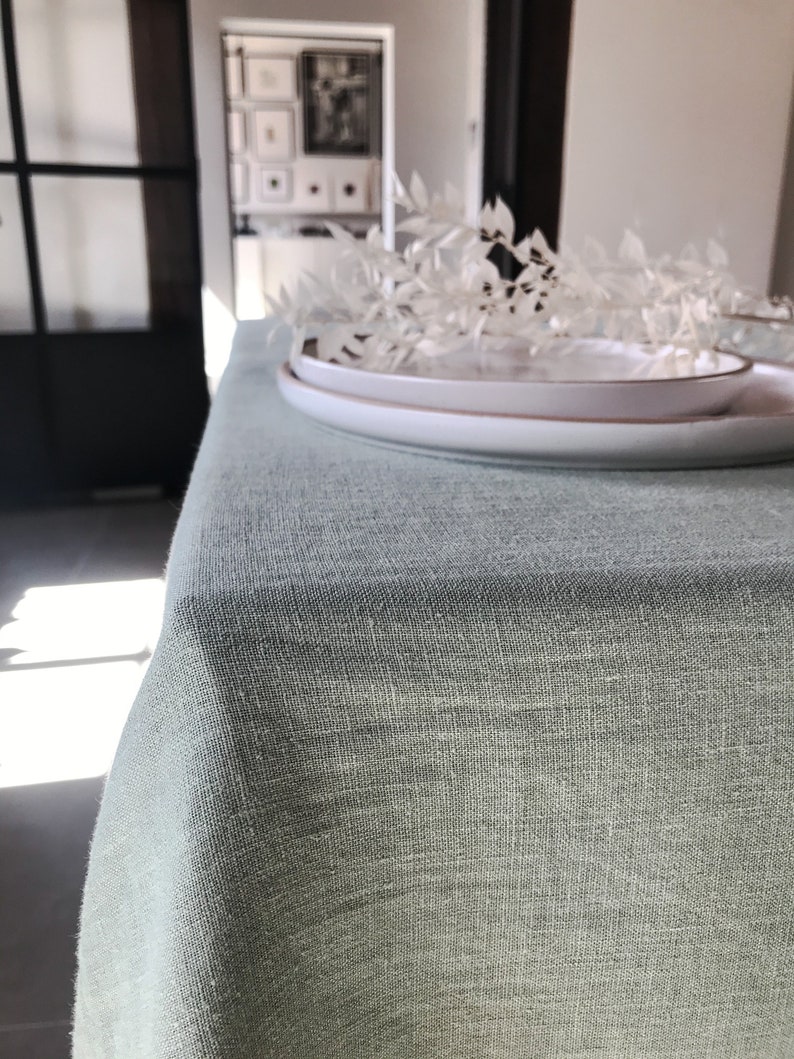 Puede incluir: Un mantel de lino verde claro con un plato blanco encima. El mantel es texturizado y tiene un brillo sutil.