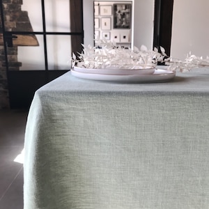 May include: A light green linen tablecloth with a white plate and white dried branches on top.