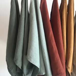 May include: Seven linen tea towels hanging on a white rod. The towels are in various shades of green, blue, red, yellow, and orange.