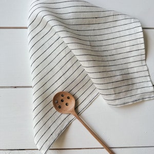 May include: A white linen kitchen towel with black stripes and a wooden slotted spoon.