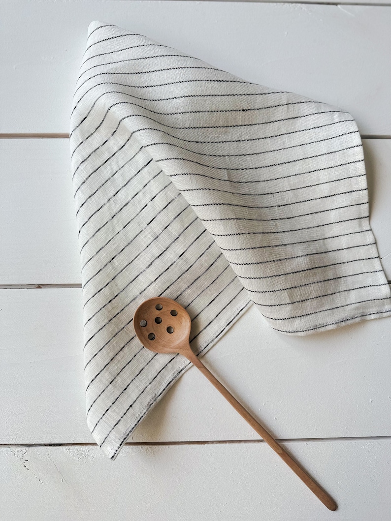 May include: A white linen kitchen towel with black stripes and a wooden slotted spoon.