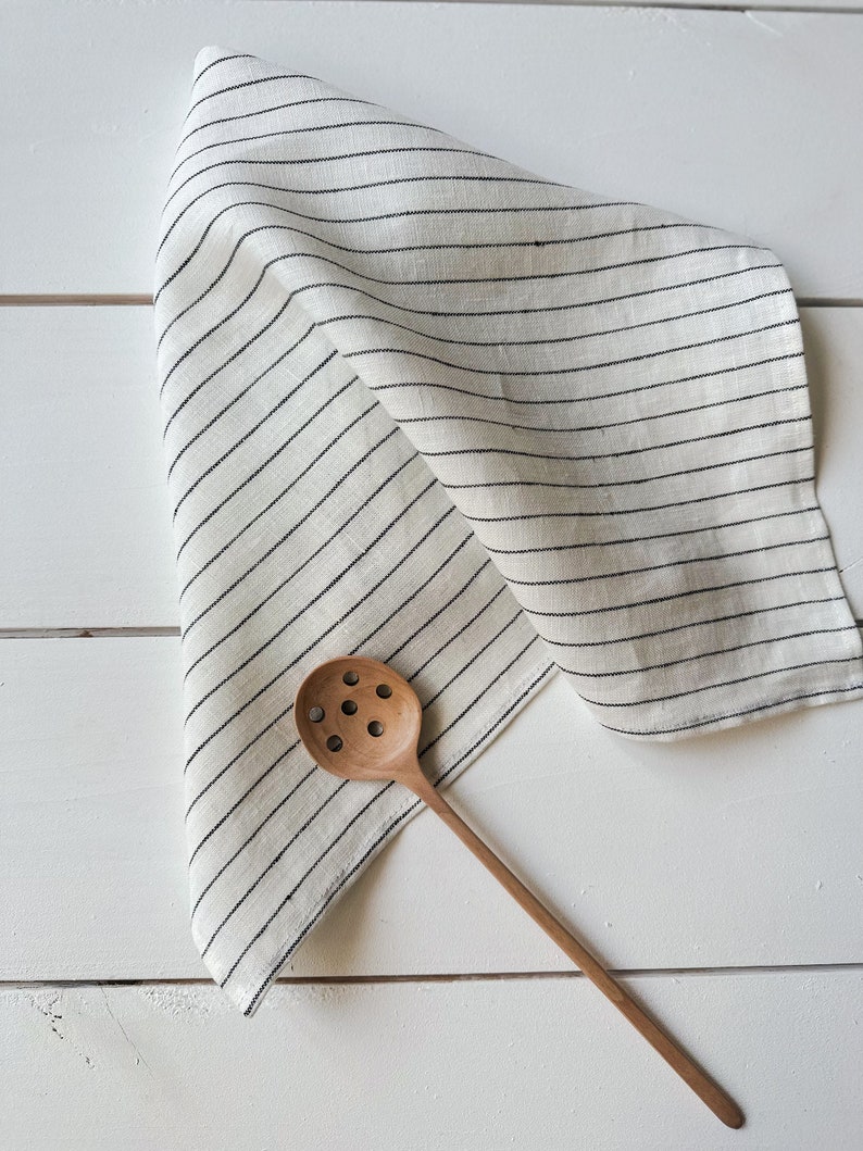 May include: A white linen kitchen towel with black stripes and a wooden slotted spoon.