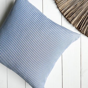 May include: A blue and white striped cushion with a square shape. The cushion is made of a soft, woven fabric.