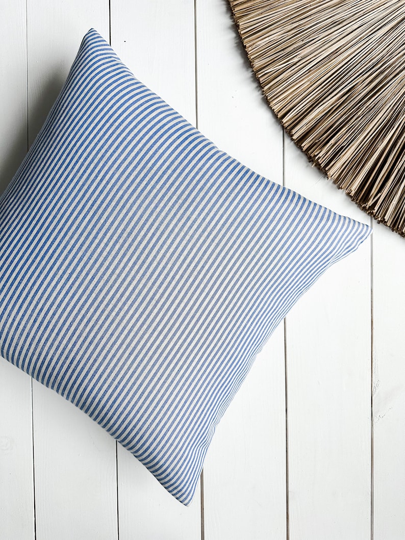 May include: A blue and white striped cushion with a square shape. The cushion is made of a soft, woven fabric.