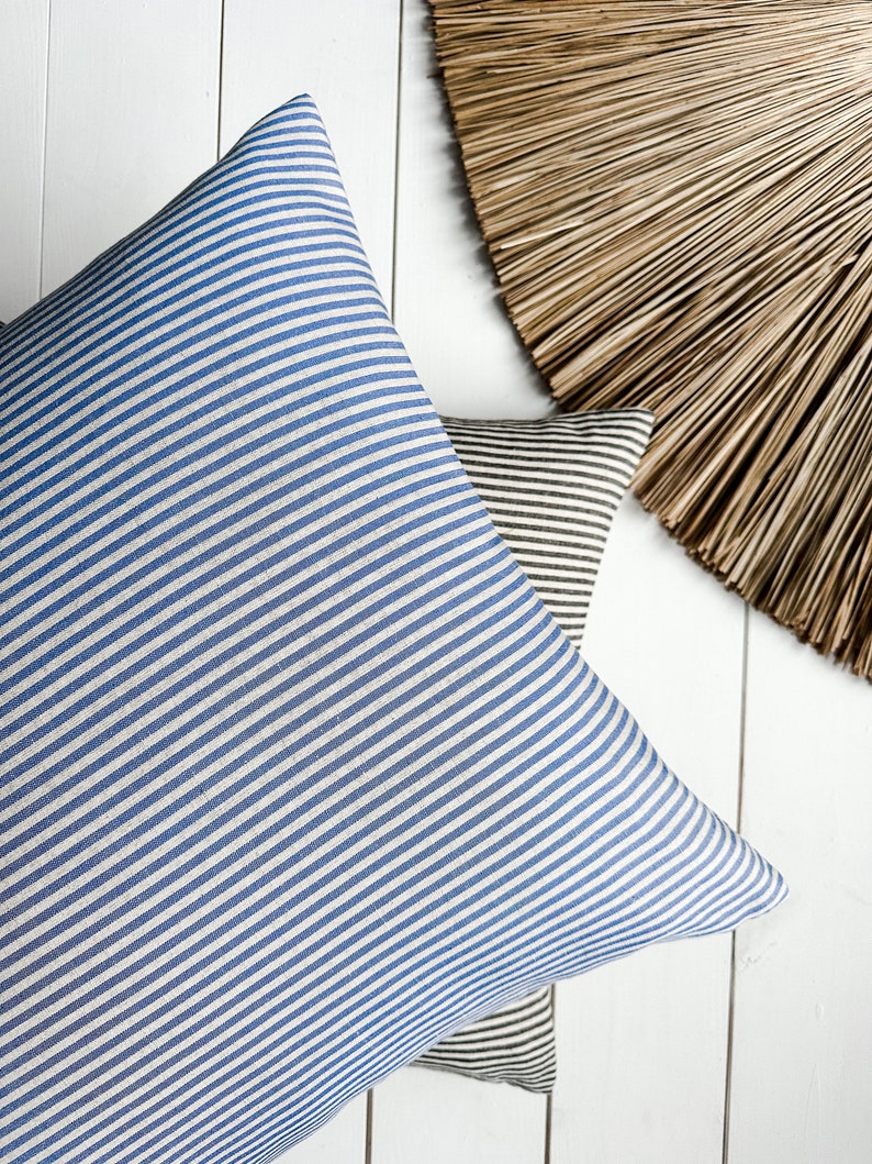 May include: Two striped cushion covers, one blue and white, and one brown and white, on a white wooden surface.