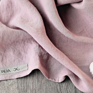 May include: A pink linen kitchen towel with a gray label that says "JAUJA" and a small white garlic clove on top of the towel.