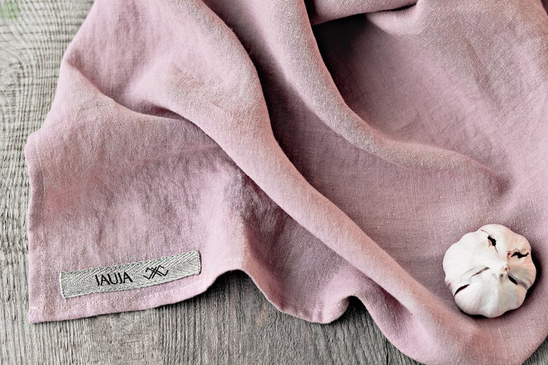 May include: A pink linen kitchen towel with a gray label that says "JAUJA" and a small white garlic clove on top of the towel.