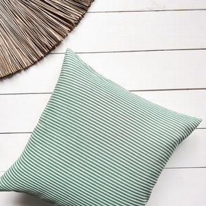 May include: A green and white striped cushion on a white wooden surface.