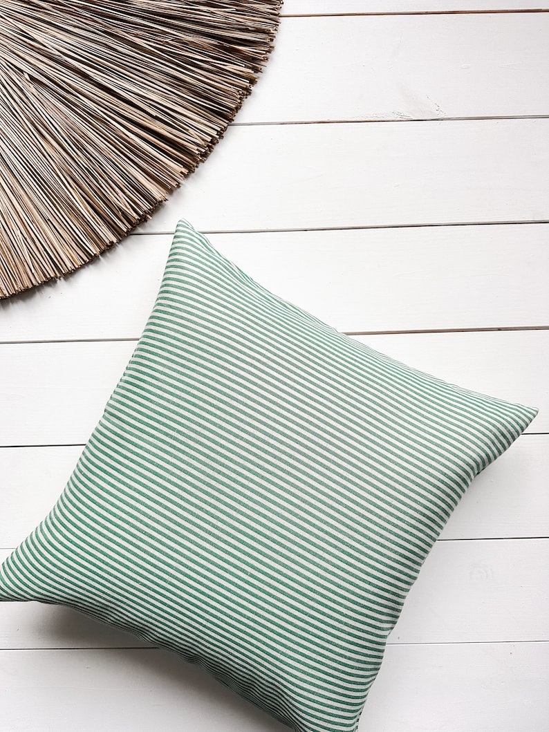 May include: A green and white striped cushion on a white wooden surface.