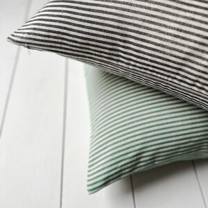 May include: Two striped throw pillows, one black and white, and one green and white, are stacked on top of each other.