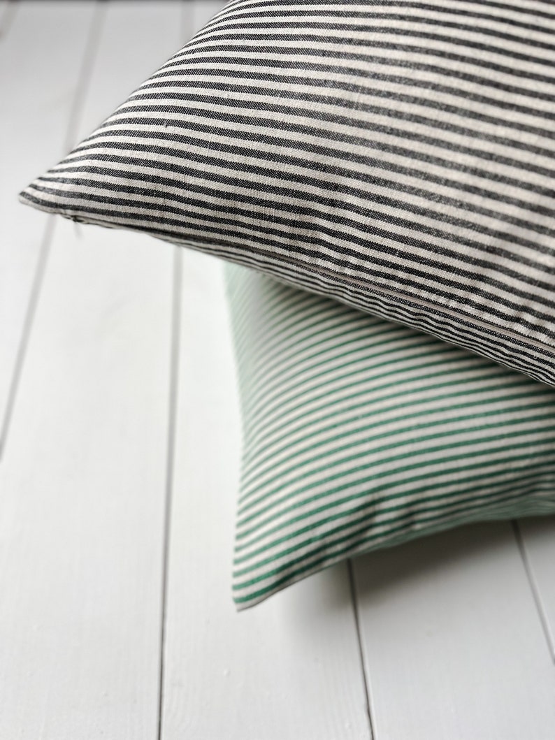 May include: Two striped throw pillows, one black and white, and one green and white, are stacked on top of each other.