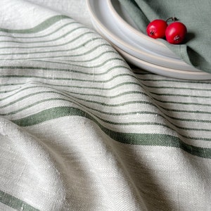 K&ouml;nnte beinhalten: Eine wei&szlig;e Tischdecke aus Leinen mit gr&uuml;nen Streifen. Die Tischdecke ist gefaltet und &uuml;ber einen Tisch gelegt. Auf einem wei&szlig;en Teller liegen zwei rote Beeren auf einer gr&uuml;nen Serviette.