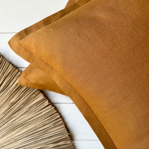 Pode incluir: Uma capa de almofada de linho marrom com uma textura sutil. A capa de almofada tem um design simples e limpo e é perfeita para adicionar um toque de calor a qualquer ambiente.