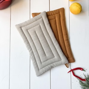 May include: Two quilted pot holders, one beige and one brown, on a white wooden surface. There are two lemons and two red chilli peppers on the surface.