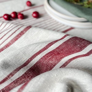 K&ouml;nnte beinhalten: Eine wei&szlig;e Tischdecke aus Leinen mit roten Streifen. Die Tischdecke ist in der Mitte gefaltet und hat ein paar rote Beeren darauf verstreut.