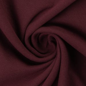 May include: Close-up of a deep burgundy fabric with a textured surface. The fabric is folded and draped, creating soft folds and curves.