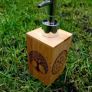 May include: A wooden soap dispenser with a silver pump top. The dispenser is decorated with a carved tree of life design and a compass with runes around it.