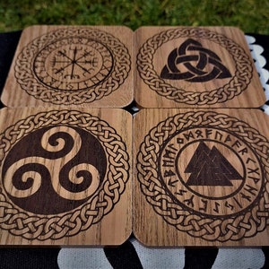 May include: Set of four wooden coasters with intricate Celtic knot designs. Each coaster features a different symbol, including a compass, a triquetra, a triskelion, and a Valknut.