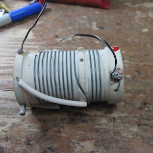 May include: A white ceramic coil with black wire wrapped around it. The coil has a white plastic tube attached to it.