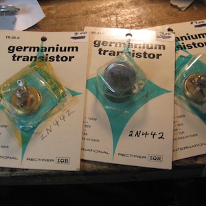 May include: Three packs of germanium transistors, each containing a different transistor. The packs are white with green accents and the text "germanium transistor" printed on them. The packs are labelled with the part number "2N442" and the price "3.00".