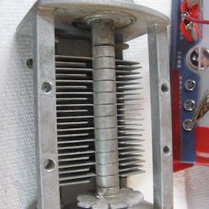 May include: A vintage silver-toned variable capacitor with a black knob. The device features multiple parallel metal plates and a central rotating shaft. The capacitor is rectangular and has a series of mounting holes.