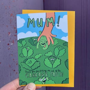 Puede incluir: Una tarjeta de felicitación con una ilustración de dibujos animados de una mano sacando una cara sonriente de un campo de coles verdes. La tarjeta dice "¡MAMÁ!" y "¡Gracias por sacarme del PARCHE DE COLES!"