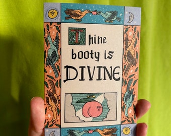 May include: A rectangular card with a whimsical illustration and the text "Thine booty is DIVINE." The artwork features a peach with a face, birds, and decorative borders in shades of orange, blue, and green. The card is held against a green background.