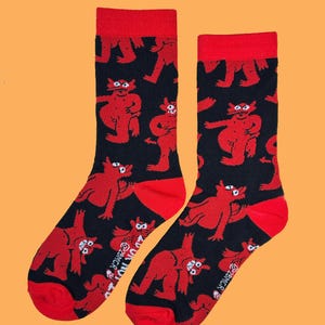 May include: A pair of black socks with a repeating pattern of red cartoon devils. The socks have red heels and toes, and red cuffs. The text "@BMCR" is printed on the side of each sock.