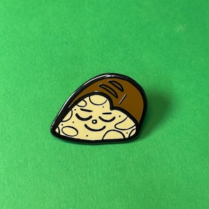 May include: A brown and yellow enamel pin shaped like a loaf of bread with a smiling face.
