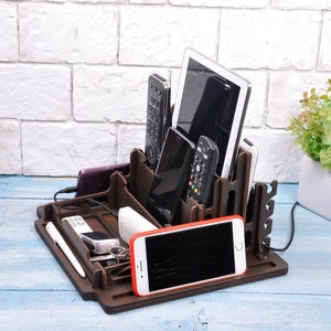 May include: A wooden organizer with multiple compartments for holding phones, remotes, and other electronics. The organizer is brown and has a natural wood finish. It is sitting on a blue surface.