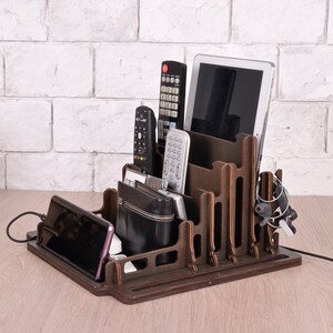 May include: A wooden organizer with multiple compartments for holding electronics, such as a tablet, phone, and remotes. The organizer is dark brown and has a natural wood finish.