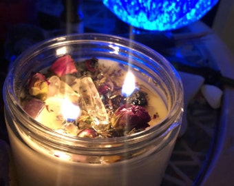 May include: A white candle with dried flowers and a clear crystal inside. The candle is lit and the flames are visible.