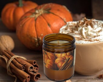 May include: A brown glass jar candle with a label featuring pumpkins and cinnamon sticks. The candle is lit, and the background includes pumpkins, a cup of whipped cream, and a bundle of cinnamon sticks, evoking a fall theme.