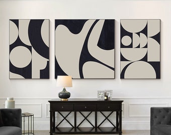 May include: Three abstract art prints with geometric shapes in black and beige colors, hanging on a white wall above a black console table with a black lamp and a coffee table with a book on it.