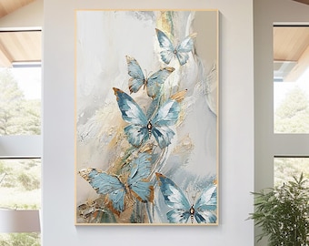 May include: A large rectangular canvas art piece featuring several blue and gold butterflies. The butterflies have detailed wing patterns and are set against a textured, abstract background with neutral tones. The artwork is framed in a gold-colored border.