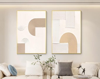 Può includere: Due dipinti astratti con sfondo bianco e forme geometriche beige. I dipinti sono incorniciati in oro e appesi a una parete bianca.