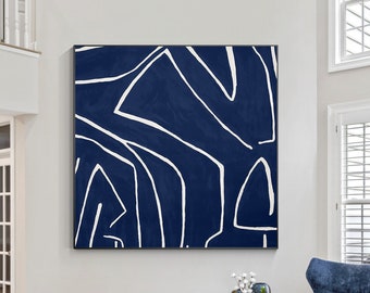 May include: A large square wall art piece featuring a deep navy blue background with bold, irregular white line patterns. The artwork is framed in a thin black border and is displayed prominently on a light-colored wall above a media console.