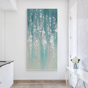 May include: Abstract painting with a teal background and white floral designs. The painting is framed and hanging on a white wall.