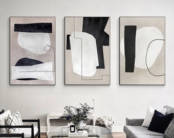 May include: Three abstract art prints with black and white geometric shapes on a beige background. The prints are framed in black and hung on a white wall.