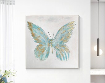 May include: A blue and gold butterfly painting on a white canvas. The butterfly has delicate wings with gold accents. The painting is framed and ready to hang.