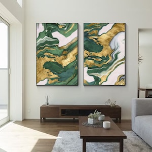 May include: Two rectangular wall art pieces featuring an abstract marble-like pattern with swirling layers of deep forest green, metallic gold, and soft white. Each canvas is framed in a thin black border, displaying fluid, organic shapes.