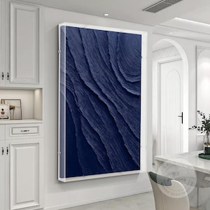 May include: A large abstract painting with a deep blue colour and a textured, layered design. The painting is framed in a clear acrylic frame and is hanging on a white wall.