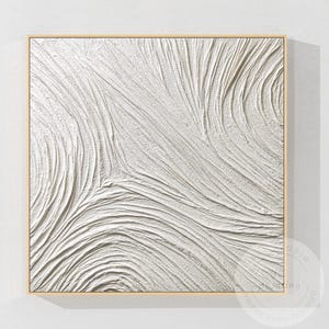 May include: Square, textured white abstract art piece in a light wooden frame. The artwork features a series of curved, flowing lines that create a sense of movement and depth. The texture appears to be thick and raised, adding a tactile element.