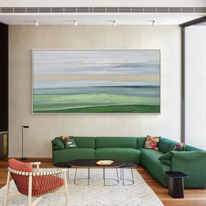 May include: Abstract landscape painting featuring shades of green, blue, and white. The painting is framed and displayed on a wall in a living room setting.