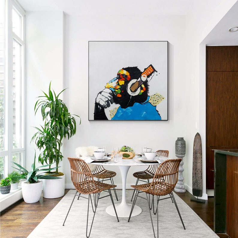 May include: A white dining table with four chairs, a painting of a monkey wearing headphones, and a potted plant in the corner.