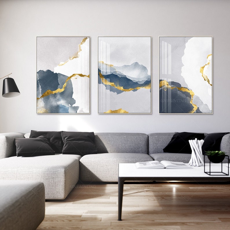 May include: Three abstract art prints with a white background and blue and gold watercolour-like designs. The prints are framed in a thin, white frame.