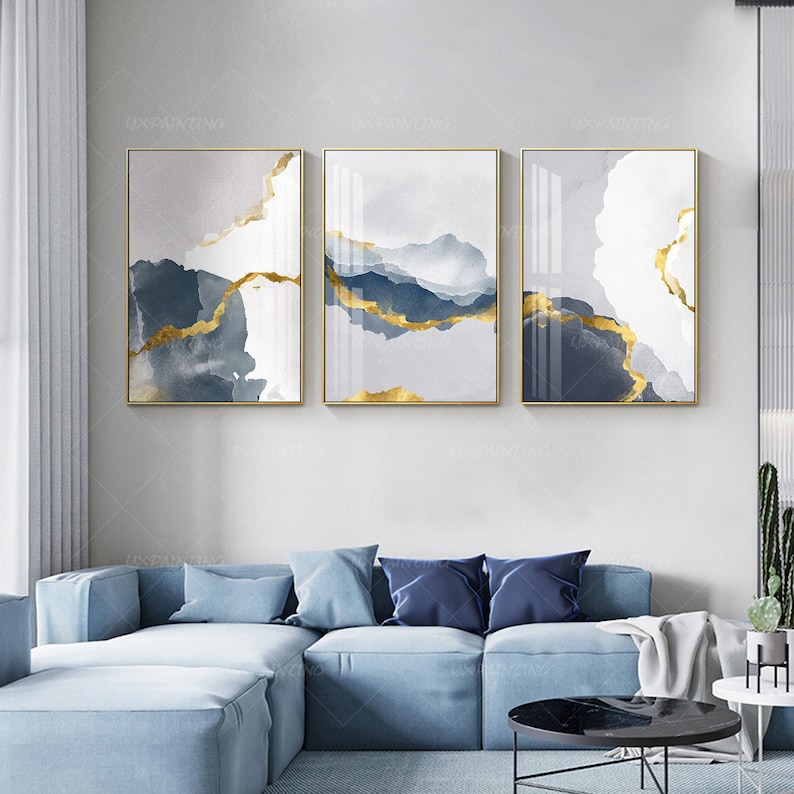 May include: Three abstract art prints with a gold and blue color scheme. The prints feature a watercolor-like background with gold accents. The prints are framed in gold.