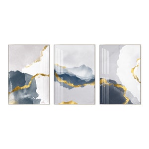 May include: A set of three abstract art prints featuring a watercolour-like design with blue and grey hues and gold accents. The prints are framed in a simple, modern style.