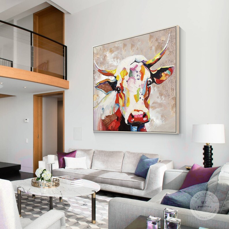 May include: A colorful abstract painting of a cow's head with a white background. The cow's head is painted in a variety of colors, including red, yellow, blue, and green. The painting is framed in a simple, modern frame.