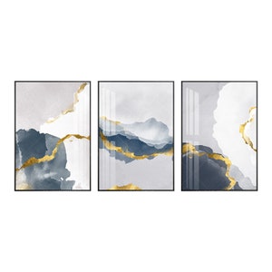 May include: Three abstract art prints with a white, grey, and blue background with gold accents. The prints are framed in black.